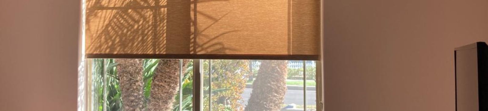 Beige roller shades partially pulled down in a bright San Diego bedroom with natural light.